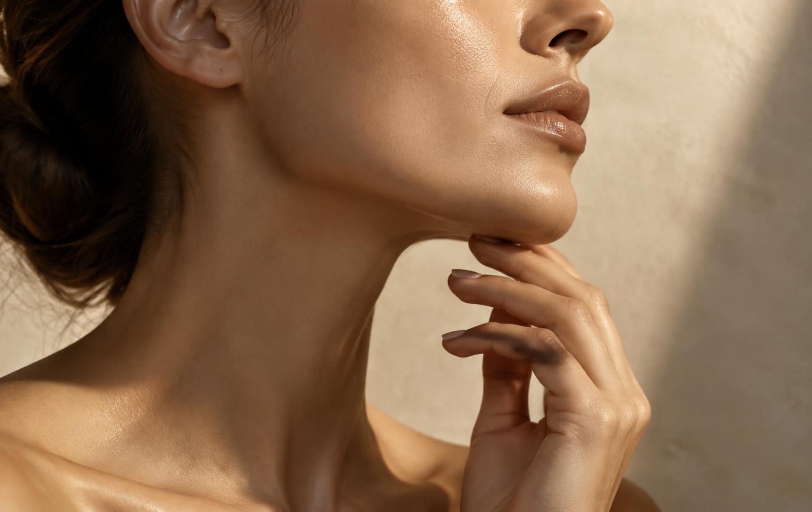 Woman touching her softly defined jawline in warm editorial light at Tula Tu Aesthetics in The Woodlands, TX